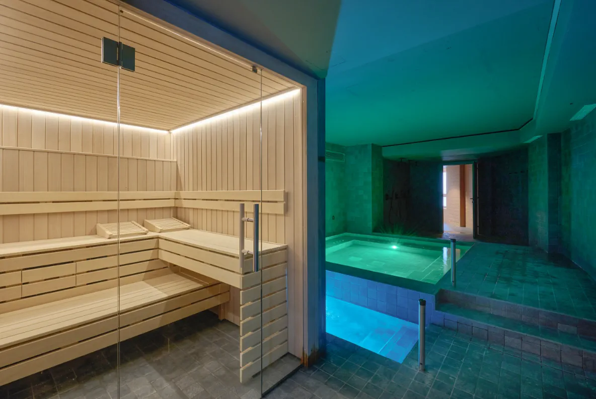 Sauna de fusta i piscina d'hidromassatge de l'spa de Casa Serras amb il·luminació blava.